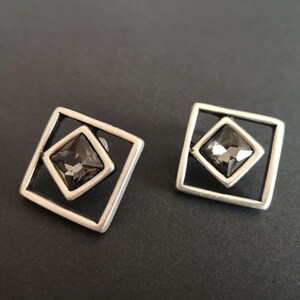 May include: A pair of silver earrings with a square frame and a dark gray crystal in the center.