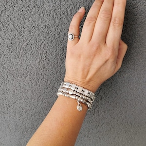 May include: A silver ring with a spiral design and three silver bracelets with square and round beads. One bracelet has a small heart charm. The jewellery is displayed against a grey background.