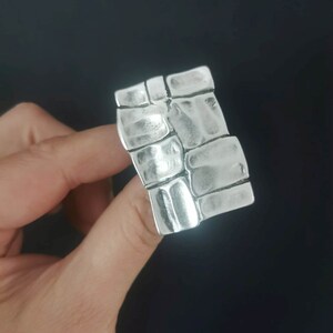 May include: A silver ring with a textured design resembling a brick wall.