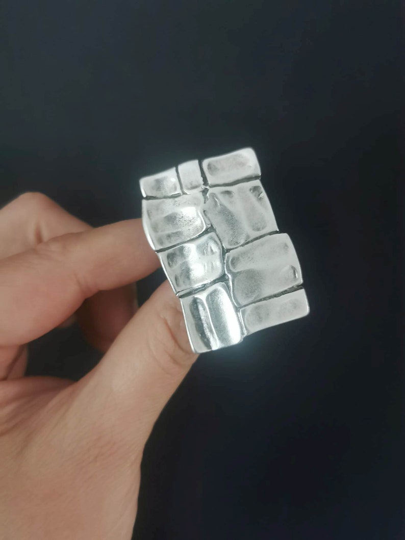 May include: A silver ring with a textured design resembling a brick wall.