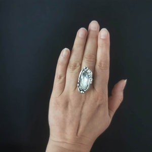 May include: A silver ring with a large, clear, oval-shaped gemstone set in a detailed, ornate design.