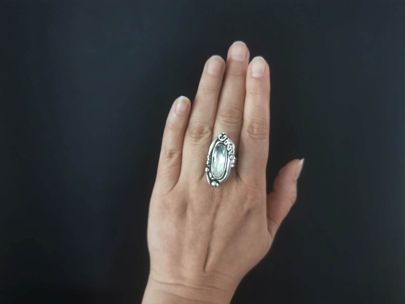 May include: A silver ring with a large, clear, oval-shaped gemstone set in a detailed, ornate design.