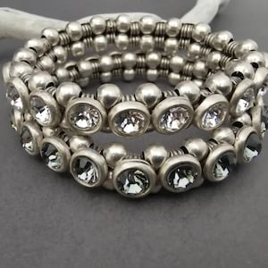 Puede incluir: Una pulsera de espiral con múltiples hileras que presenta una serie de cuentas metálicas redondas de tono plateado y espaciadores estriados. El diseño incorpora cristales circulares facetados transparentes en engastes plateados.