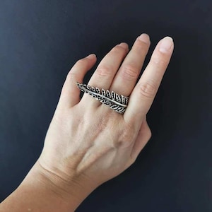 Op de afbeelding: Een zilveren ring met een bladontwerp. De ring wordt gedragen aan de middelvinger van een hand.