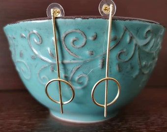 May include: A pair of gold earrings with a simple circle design. The earrings are hanging from a bowl.