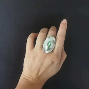 Puede incluir: Un anillo de plata con un engaste ovalado que presenta una piedra preciosa verde.
