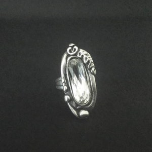 A silver plated ring with an oval-shaped clear crystal set in a detailed design.
