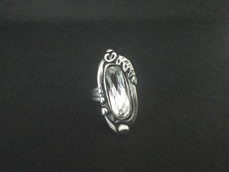 A silver plated ring with an oval-shaped clear crystal set in a detailed design.