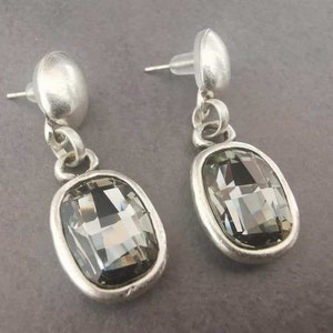 May include: A pair of silver dangle earrings with a dark gray crystal in a rectangular shape.