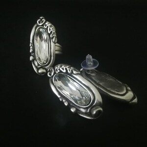 May include: A pair of silver earrings with clear crystal stones set in ornate silver settings. The earrings have a post back closure.