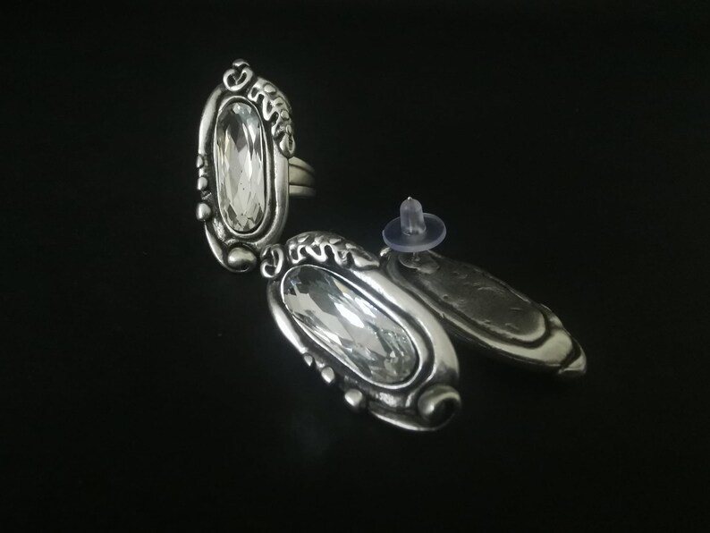 May include: A pair of silver earrings with clear crystal stones set in ornate silver settings. The earrings have a post back closure.