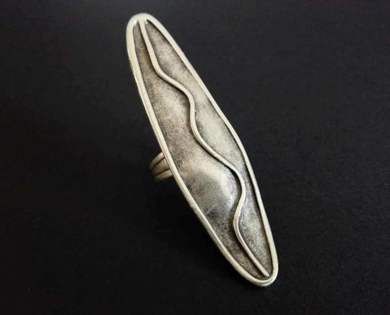 May include: A silver ring with a wavy design on the face. The ring is oval shaped and has a textured finish.