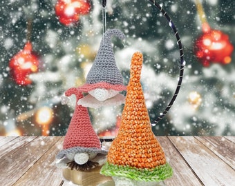 May include: Three crocheted gnomes hanging from a black metal ring. The gnome on the left is pink with a white beard, the gnome in the middle is gray with a white beard, and the gnome on the right is orange with a green trim and a white beard.