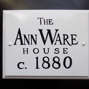May include: White wooden sign with black lettering that reads "The Ann Ware House c. 1880".