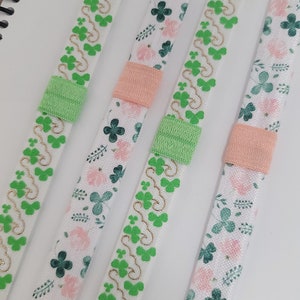 May include: Four green and white patterned ribbon with gold accents. The ribbon has a green elastic band on each end.