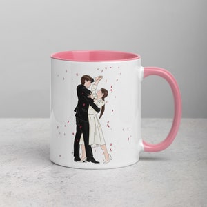 Puede incluir: Taza de cerámica blanca con borde y asa de color rosa. La taza presenta una ilustración en blanco y negro de una pareja bailando con confeti cayendo a su alrededor.