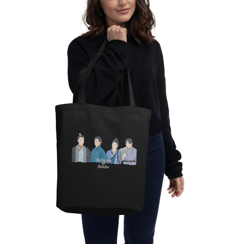 May include: Black tote bag with a print of four characters from the TV show "Alchemy of Souls". The characters are wearing traditional Korean clothing. The text "Alchemy of Souls" is printed in white below the characters.