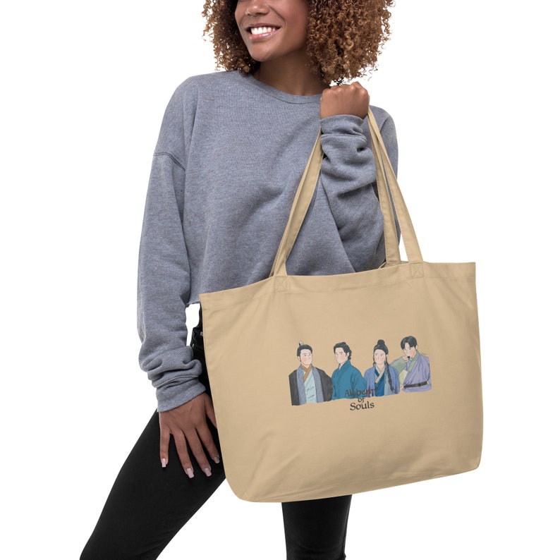 May include: A beige tote bag with a graphic of five people in traditional clothing. The text "Alchemy of Souls" is printed below the graphic.
