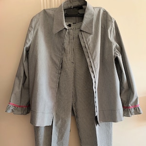 May include: A black and white gingham patterned shirt and pants set. The shirt has a collar and long sleeves with pink trim. The pants have a straight leg and are cropped.
