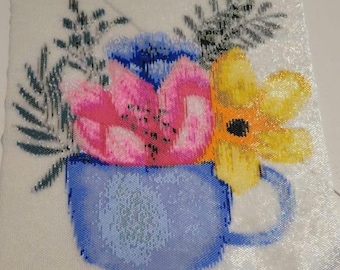 May include: A blue ceramic mug with a pink, yellow, and blue floral arrangement. The flowers are in a stylized design and the mug has a handle.