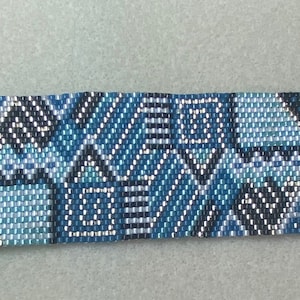 Puede incluir: Un brazalete de cuentas azul, negro y blanco con un cierre y una cadena plateados. El brazalete presenta un patrón geométrico.