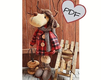 May include: A plush reindeer doll wearing a red and black plaid coat, a gray scarf, and brown boots. The doll is standing next to a wooden sled and a spool of twine. The image includes the text "PDF".