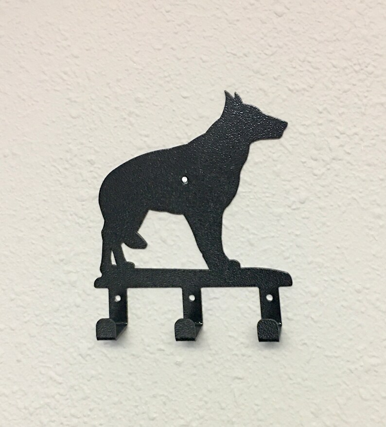 Puede incluir: Llavero de metal negro montado en la pared con la silueta de un perro pastor alem&aacute;n. El llavero tiene tres ganchos debajo de la silueta del perro, perfectos para colgar llaves u objetos peque&ntilde;os. El perro est&aacute; de pie.