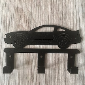 Puede incluir: Porta llaves de metal negro con forma de coche con tres ganchos.