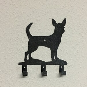 Puede incluir: Porta llaves de metal negro con forma de silueta de chihuahua con tres ganchos.