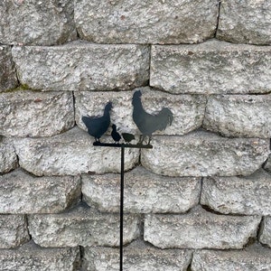 May include: Black metal silhouette of a rooster and three chickens on a metal stake. The stake is inserted into the ground. The silhouette is a garden decoration.