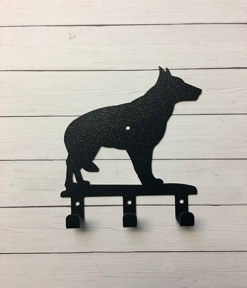 Puede incluir: Un llavero de metal negro con la silueta de un perro pastor alem&aacute;n. El llavero tiene tres ganchos debajo de la forma del perro, perfectos para colgar llaves u objetos peque&ntilde;os. El perro est&aacute; de pie sobre una barra horizontal.