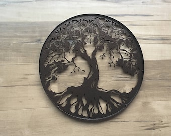 May include: A metal wall art piece in the shape of a tree of life. The tree is dark brown and has a detailed design with branches and roots. The background is a light brown wood.