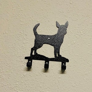 Puede incluir: Porta llaves de metal negro con forma de silueta de perro Chihuahua. El soporte tiene tres ganchos para colgar llaves.