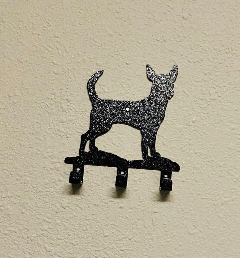Puede incluir: Porta llaves de metal negro con forma de silueta de perro Chihuahua. El soporte tiene tres ganchos para colgar llaves.
