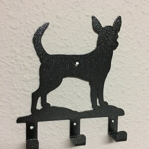 Puede incluir: Gancho para llaves de metal negro con una silueta de un perro Chihuahua. El gancho tiene tres ganchos para colgar llaves u otros art&iacute;culos.