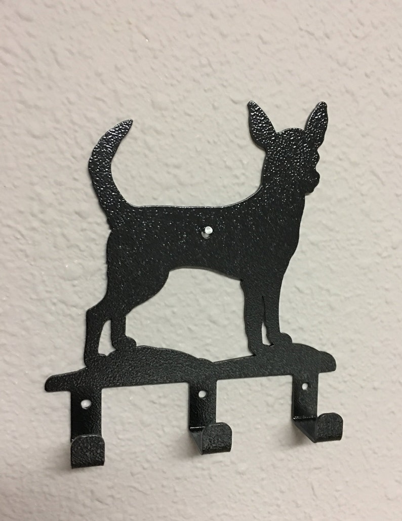 Puede incluir: Gancho para llaves de metal negro con una silueta de un perro Chihuahua. El gancho tiene tres ganchos para colgar llaves u otros art&iacute;culos.