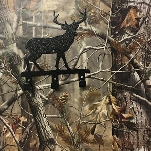 Op de afbeelding: Zwarte metalen hert silhouet sleutelhaak met drie haken. De haak is gemonteerd op een camouflage achtergrond.
