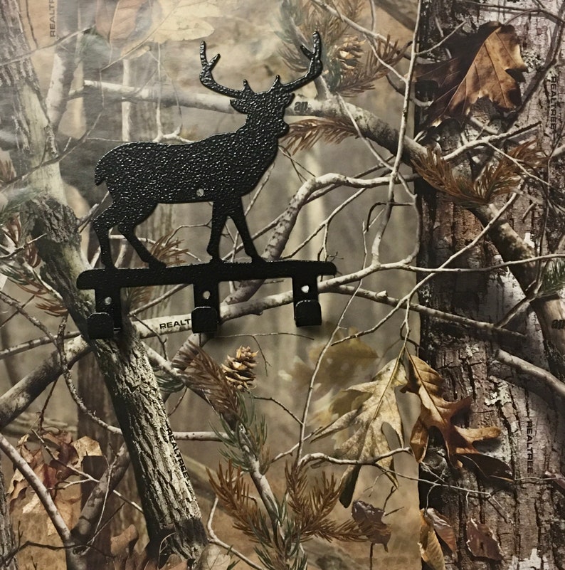 Op de afbeelding: Zwarte metalen hert silhouet sleutelhaak met drie haken. De haak is gemonteerd op een camouflage achtergrond.