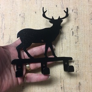 Op de afbeelding: Zwarte metalen sleutelhanger in de vorm van een hert silhouet met twee haken. Het hert staat op een metalen basis.