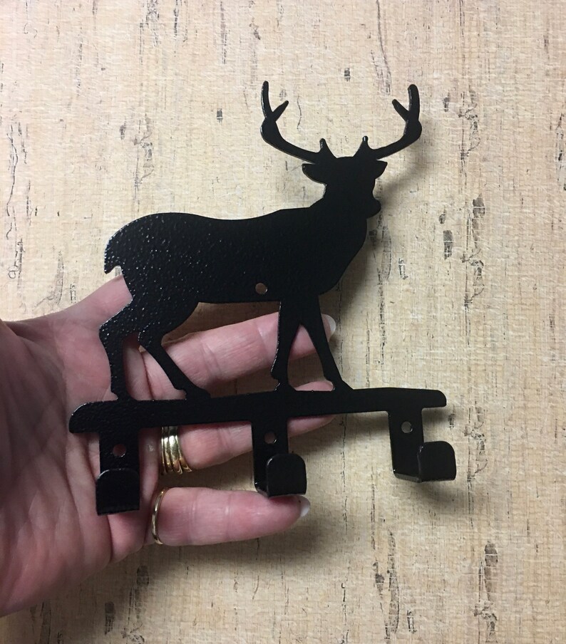 Op de afbeelding: Zwarte metalen sleutelhanger in de vorm van een hert silhouet met twee haken. Het hert staat op een metalen basis.