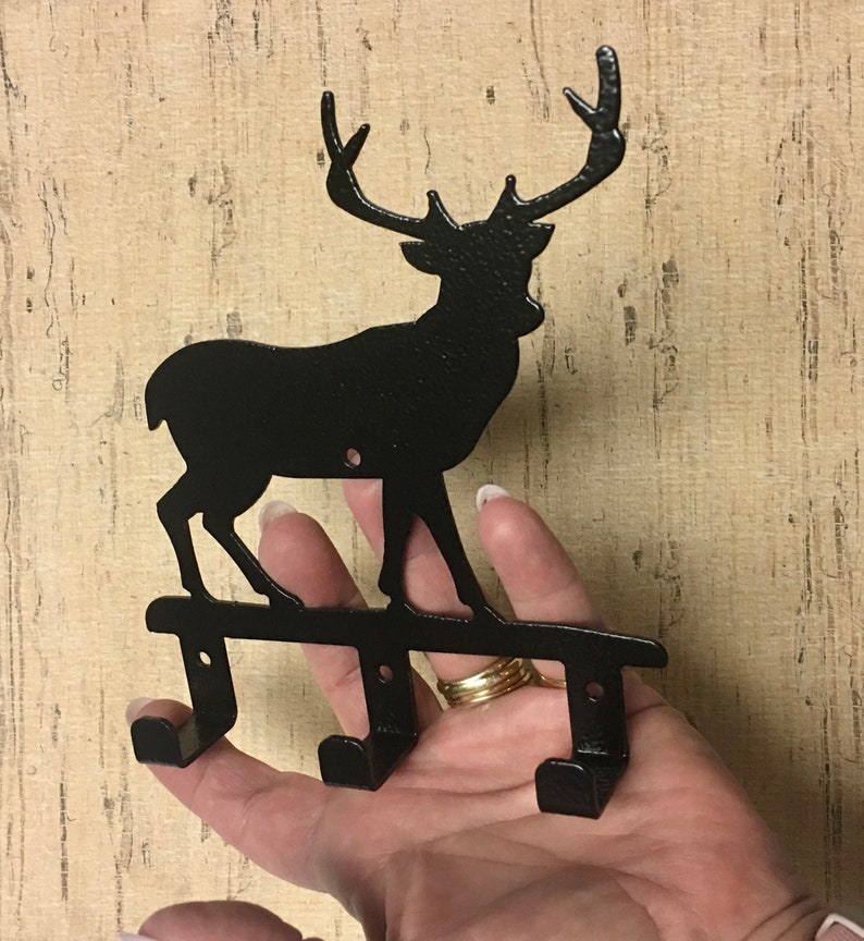 Op de afbeelding: Zwarte metalen hert silhouet wandhaak met drie haken. Het hert staat op een metalen basis.