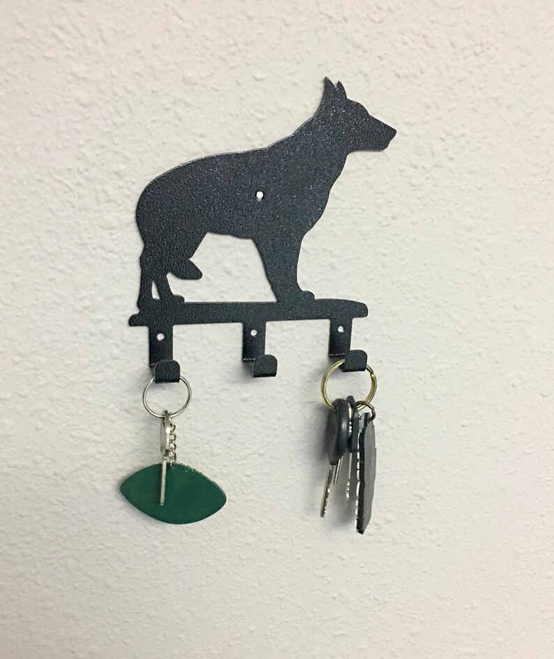 Puede incluir: Llavero de metal negro con la silueta de un perro. El llavero tiene tres ganchos y est&aacute; montado en una pared blanca. Una etiqueta de llave ovalada verde y un juego de llaves cuelgan de los ganchos.
