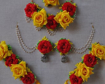 Könnte beinhalten: Ein Set aus gelbem und rotem Blumen-Schmuck, bestehend aus einer Halskette, Ohrringen und zwei Armbändern. Der Schmuck ist aus Stoffblumen gefertigt und hat eine Perlen- und Goldkette.