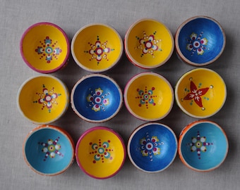 May include: Twelve small, round wooden bowls arranged in a grid. Each bowl features a unique, hand-painted dot mandala pattern in vibrant colors including yellow, blue, pink, and red. The interiors are painted in solid yellow or blue hues.