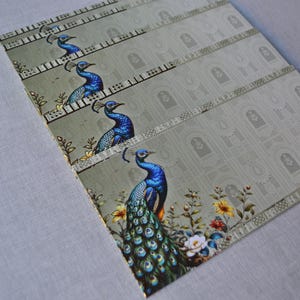 May include: A rectangular sheet of paper featuring four repeating illustrations of a blue peacock. The design includes a light green background with a subtle pattern of arched doorways and floral elements in yellow, white, and red near the bottom.