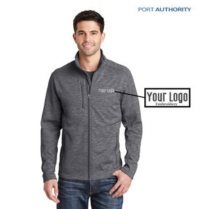 May include: A gray fleece jacket with a zipper closure and two zippered pockets. The jacket has a subtle heather pattern and the text "Your Logo" embroidered on the left chest.