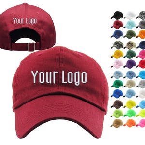 May include: A maroon baseball cap featuring the white text Your Logo embroidered on the front and back. The cap has a curved brim and an adjustable strap with a metal buckle. A grid of thirty-six additional baseball caps in various colors is shown.