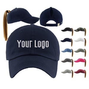 May include: A navy blue baseball cap with a ponytail hole in the back. The cap has a white embroidered logo that says "Your Logo".