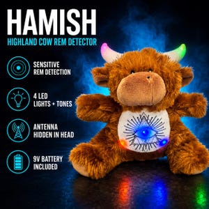 Op de afbeelding: Een bruine pluche Highland-koe met oplichtende veelkleurige hoorns en een witte buikvlek met een zwart oog-in-driehoek-motief. Het speelgoed bevat 4 led-lampjes, tonen, een in het hoofd verborgen antenne en een meegeleverde 9V-batterij.
