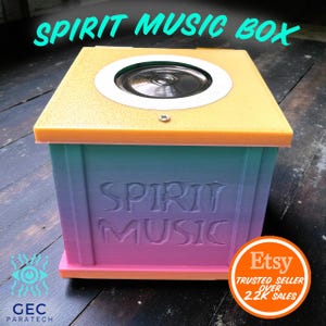 Puede incluir: Una caja de música cuadrada con un altavoz en la parte superior. La caja tiene un degradado de azul, morado y rosa, con las palabras "SPIRIT MUSIC" en relieve en la parte delantera. La parte superior es amarilla con un borde naranja. Se ve una insignia de Etsy.